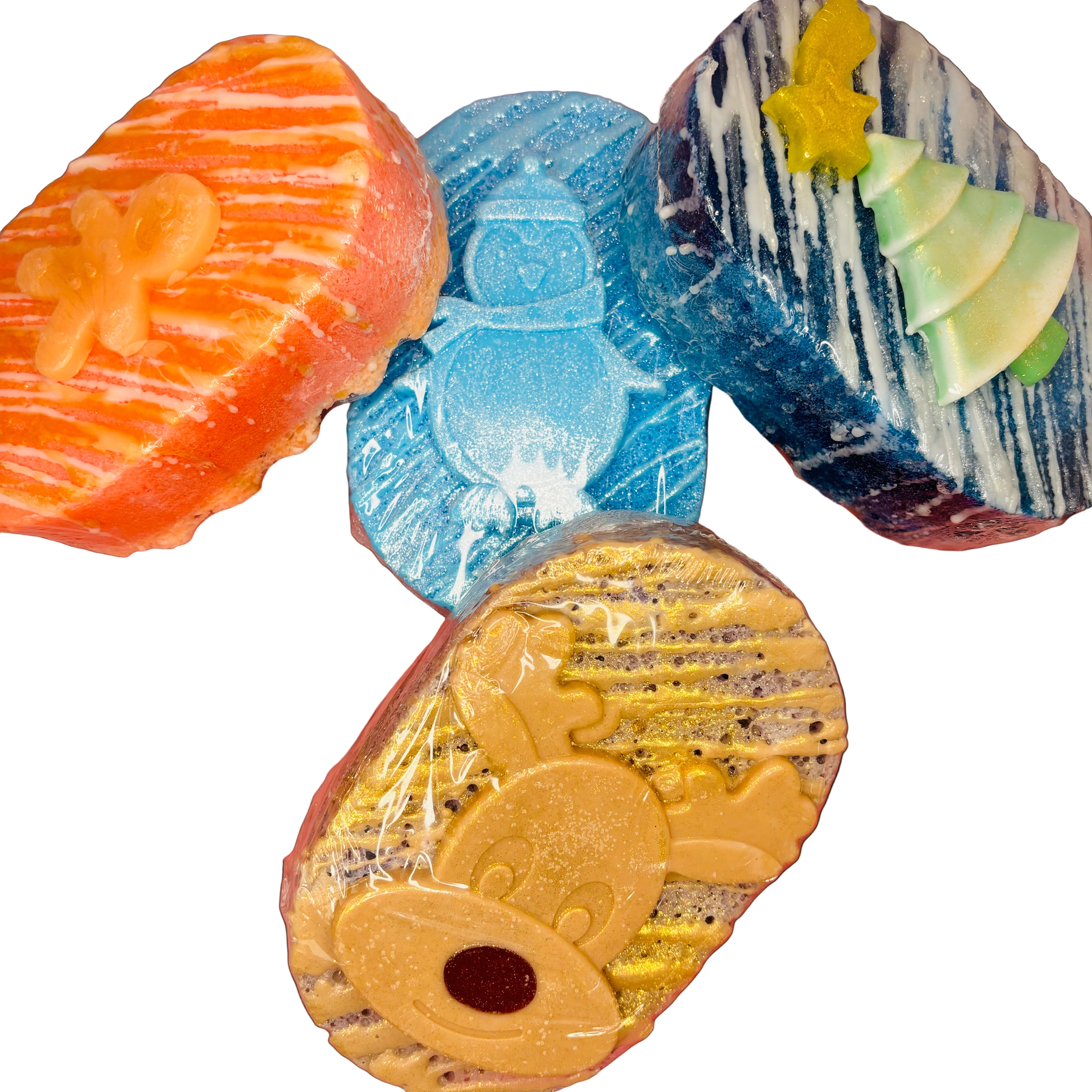 Four vibrant soap sponges from Scented Aromas, including a Gingerbread Man Soap, with festive designs featuring gingerbread, penguin, tree, and reindeer shapes—offer a luxurious lather. These are creatively displayed against a pink background.