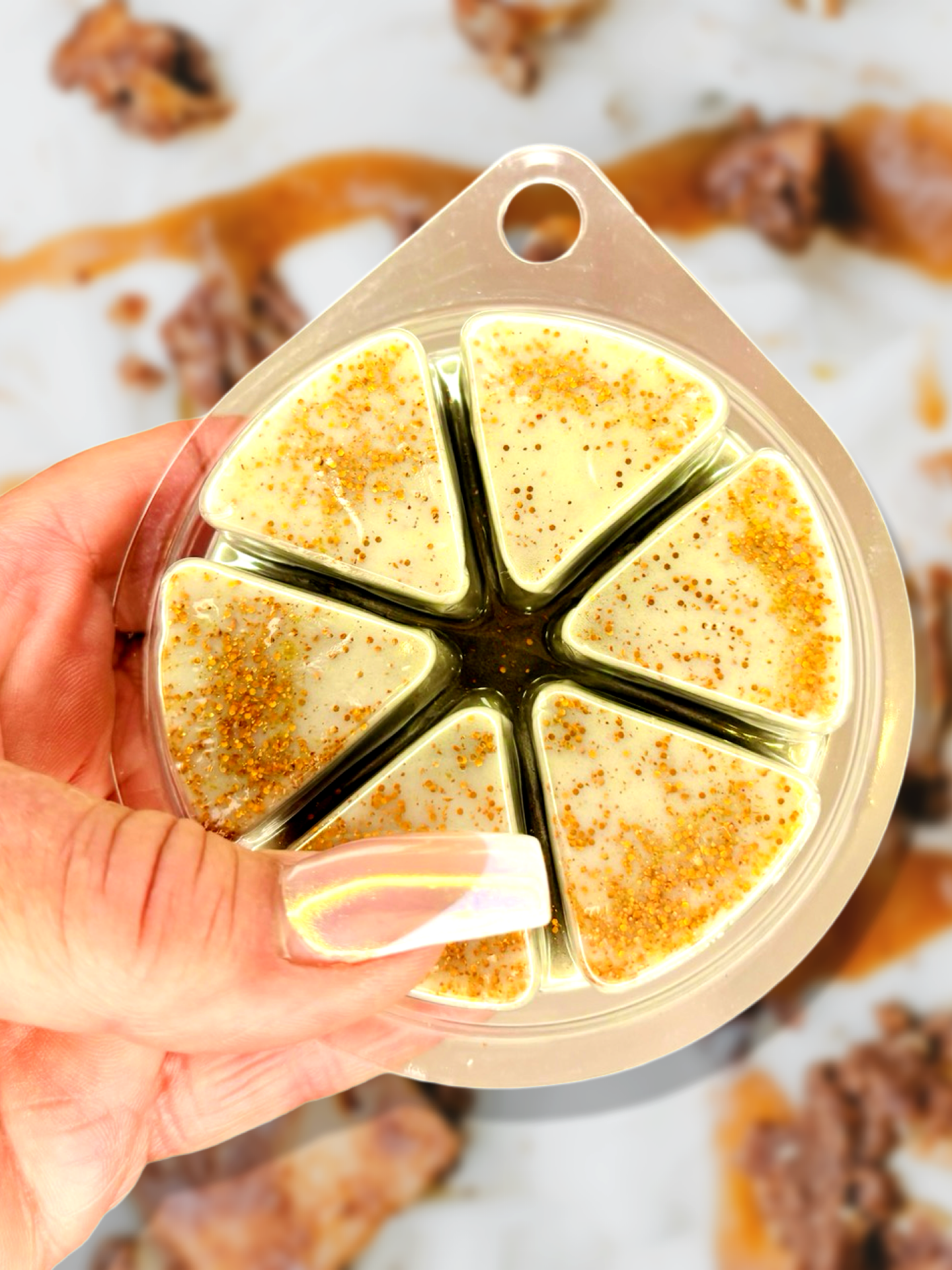 A hand holds a round container with six triangular compartments filled with seasoning, set against a backdrop of brown and white textures, reminiscent of the cozy charm provided by The Soap Gal x Nutty Fudge Wax Melt 85g, which offers a long-lasting fragrance.