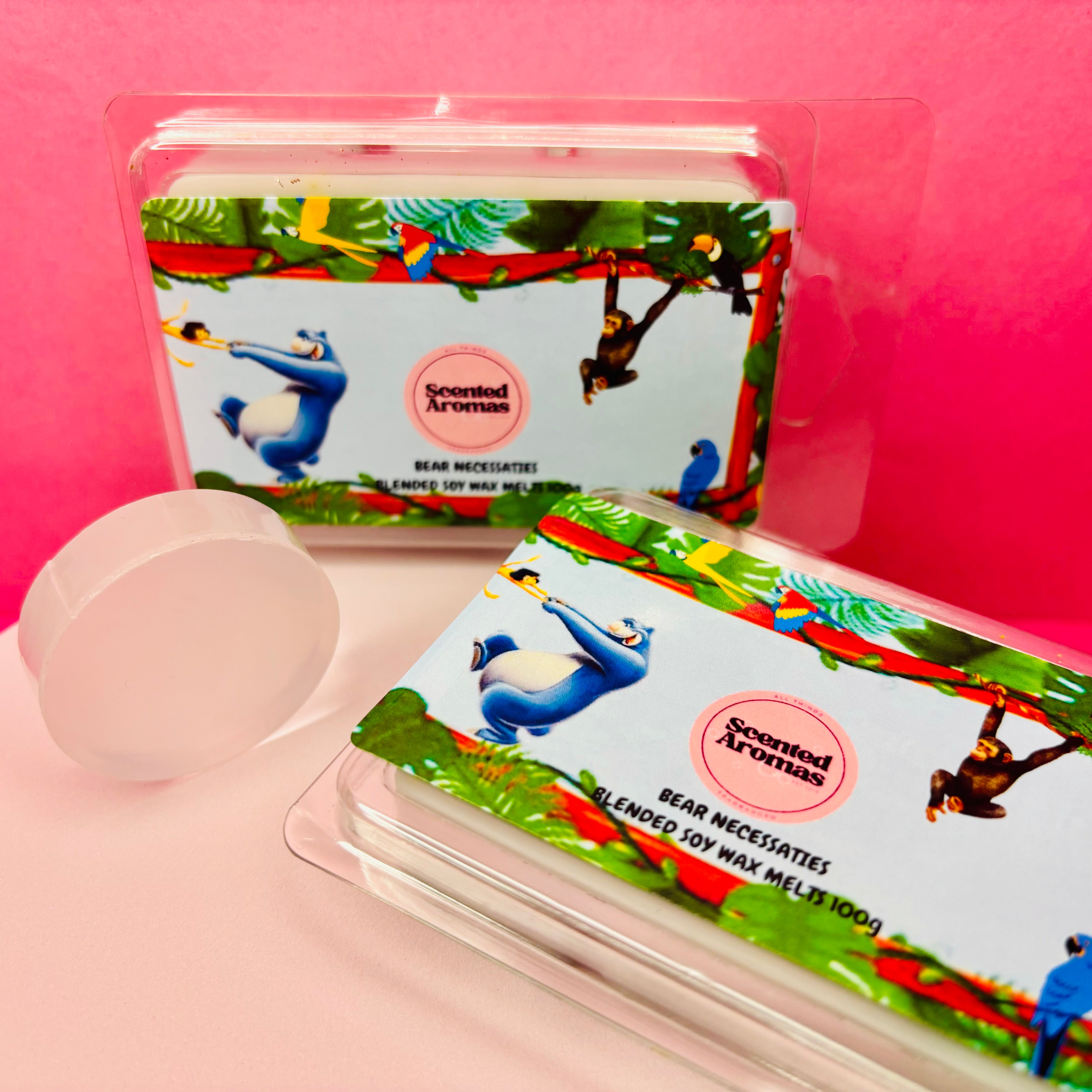 Two packs of "All You Need Is the Absolute Necessities" luxury vegan soy wax melts by The Soap Gal x, infused with essential oils and featuring a jungle theme, are displayed against a pink background.