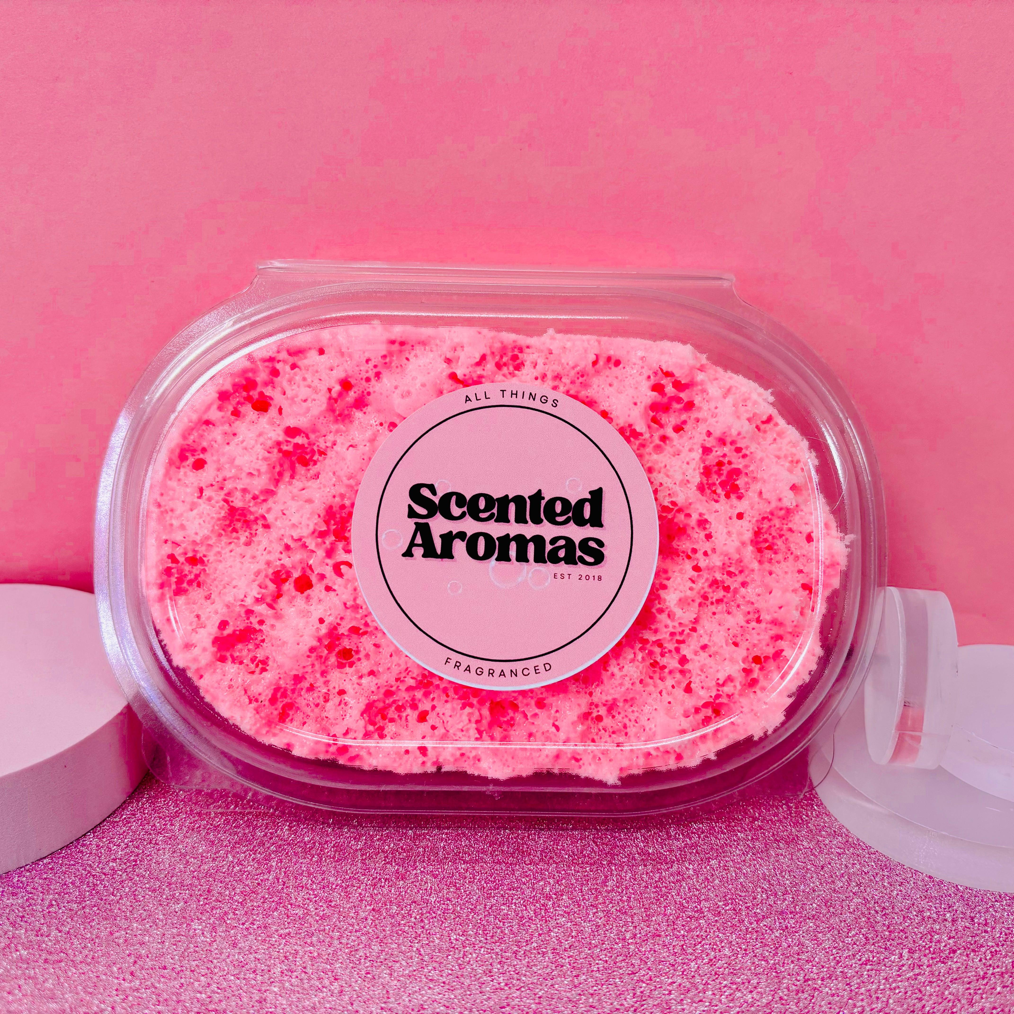 A pink scented sponge by Scented Aromas sits gracefully in a clear plastic case, nestled in a soft pink setting—ideal for the Mothers Day Gift Set Bundle of 5 beauty and home fragrance products.