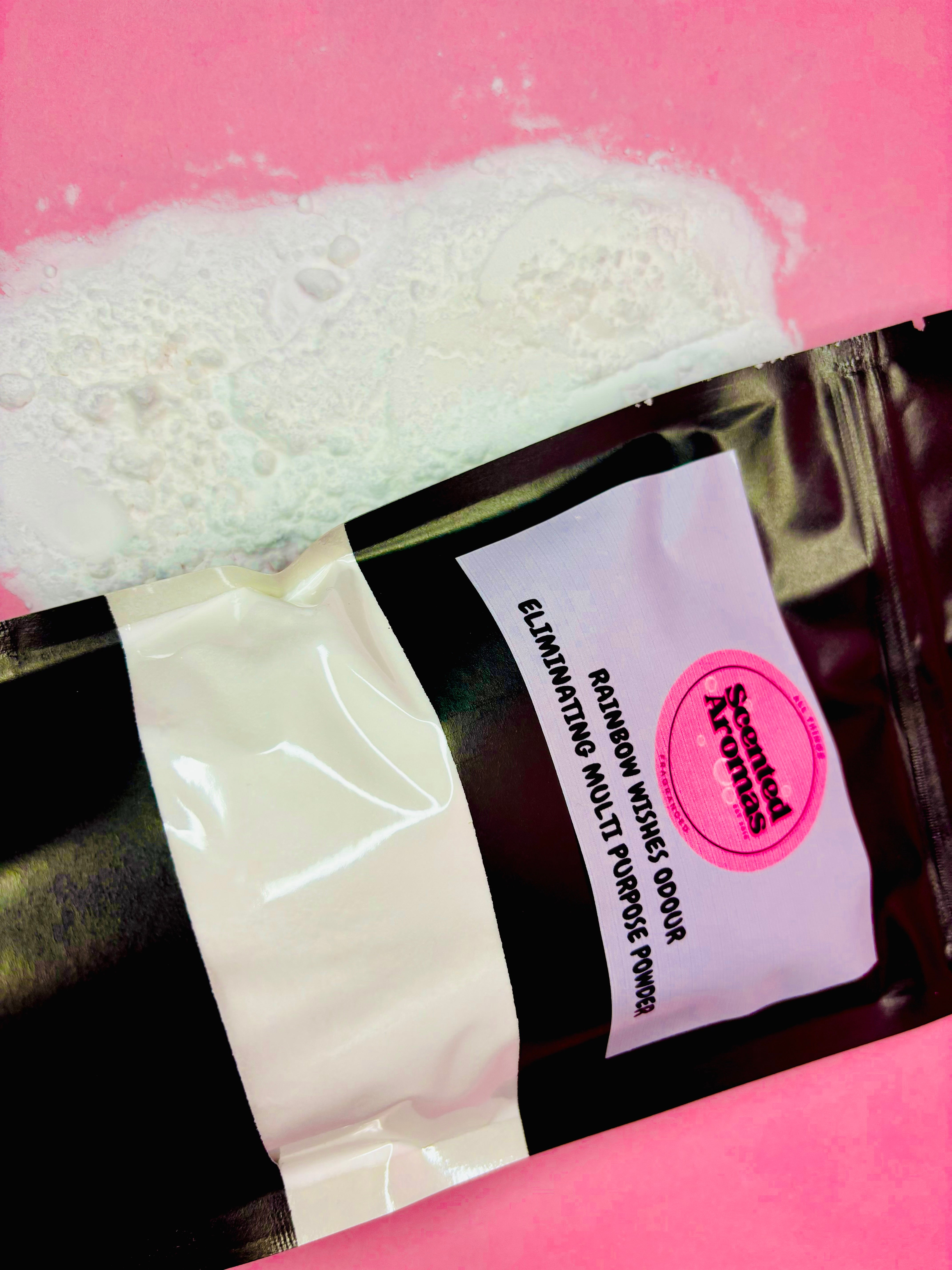 A black pouch of "Rainbow Wishes" Multi Purpose Odour Eliminating Powder from The Soap Gal x rests on a pink surface, its fruity scent wafting from the spilled powder nearby.