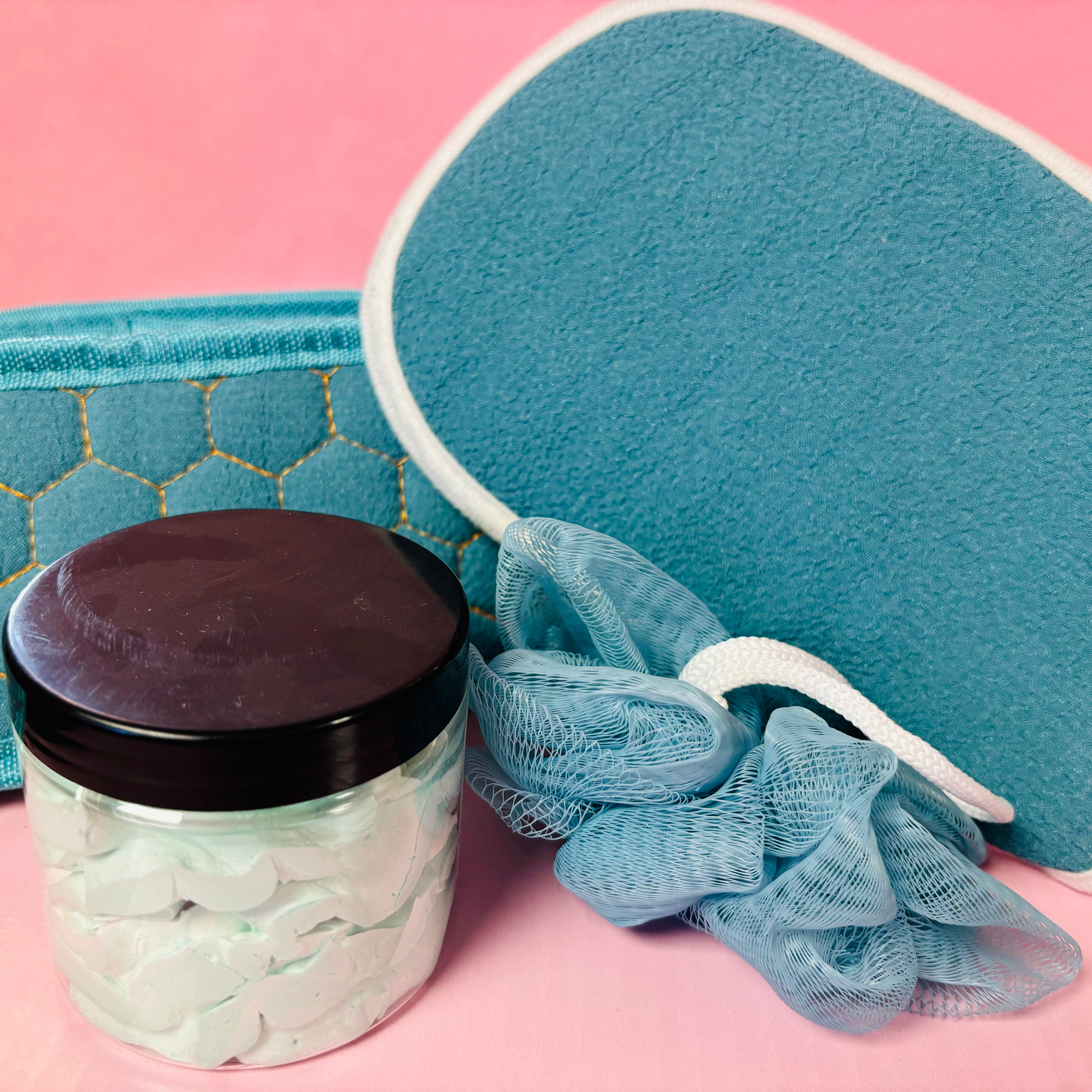 Scented Aromas' blue bath and body gift set includes whipped soap, an exfoliating mitt, a sponge, and a storage basket on a pink background.